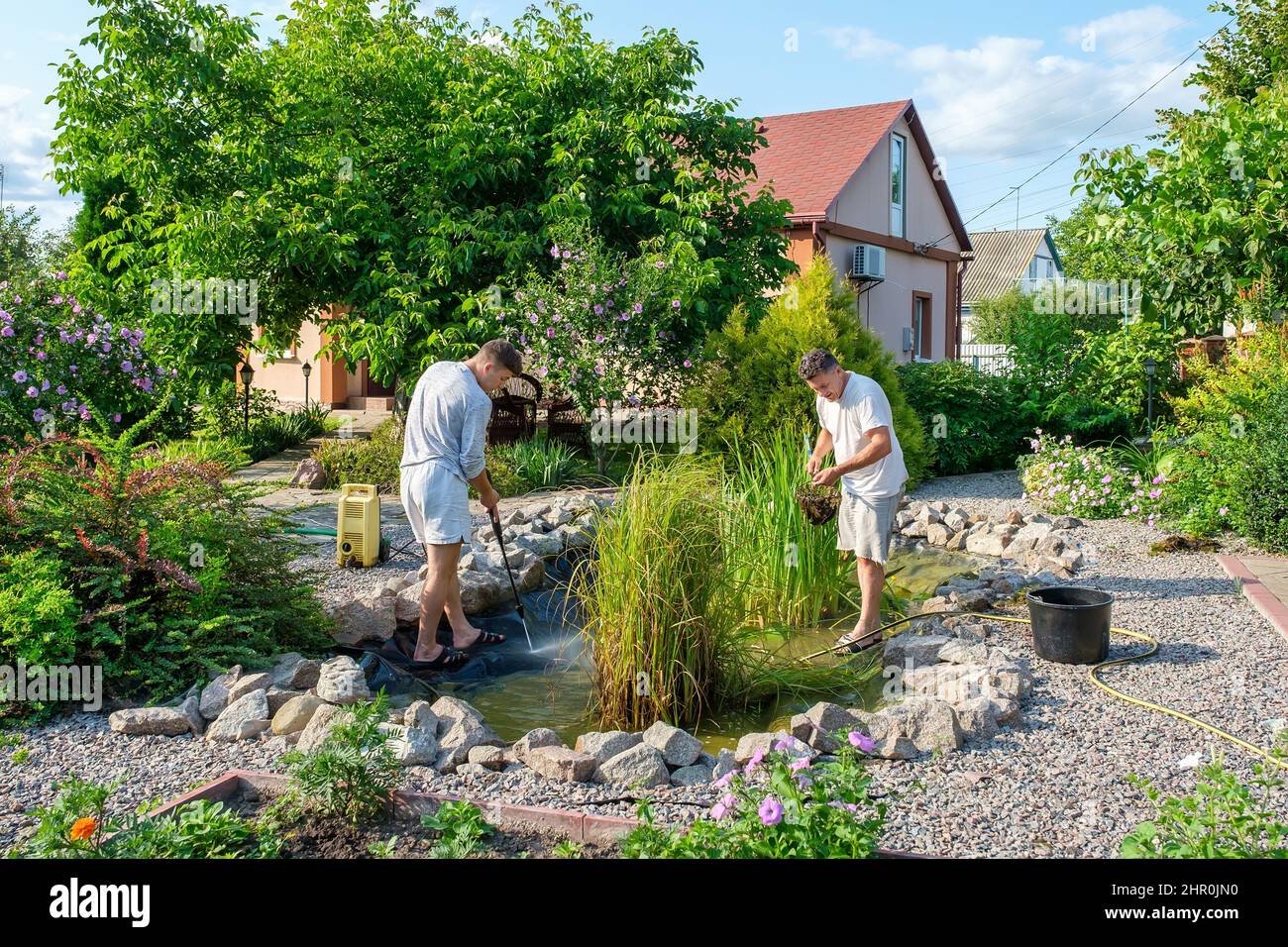 Father and son cleaning garden pond bottom with highpressure washer