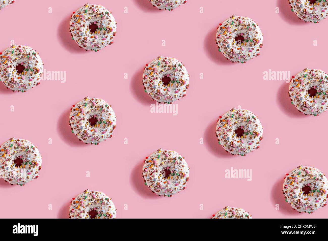 Delicious glazed donuts on the pink table background. Repeating pattern, top view, close up. Stock Photo