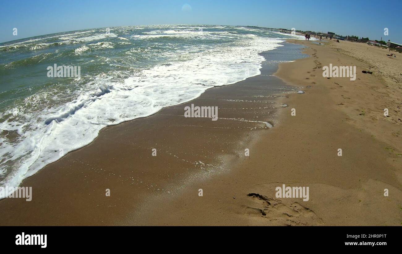 Sea wave with white foam rolls over sandy shore of beach. Top view ...