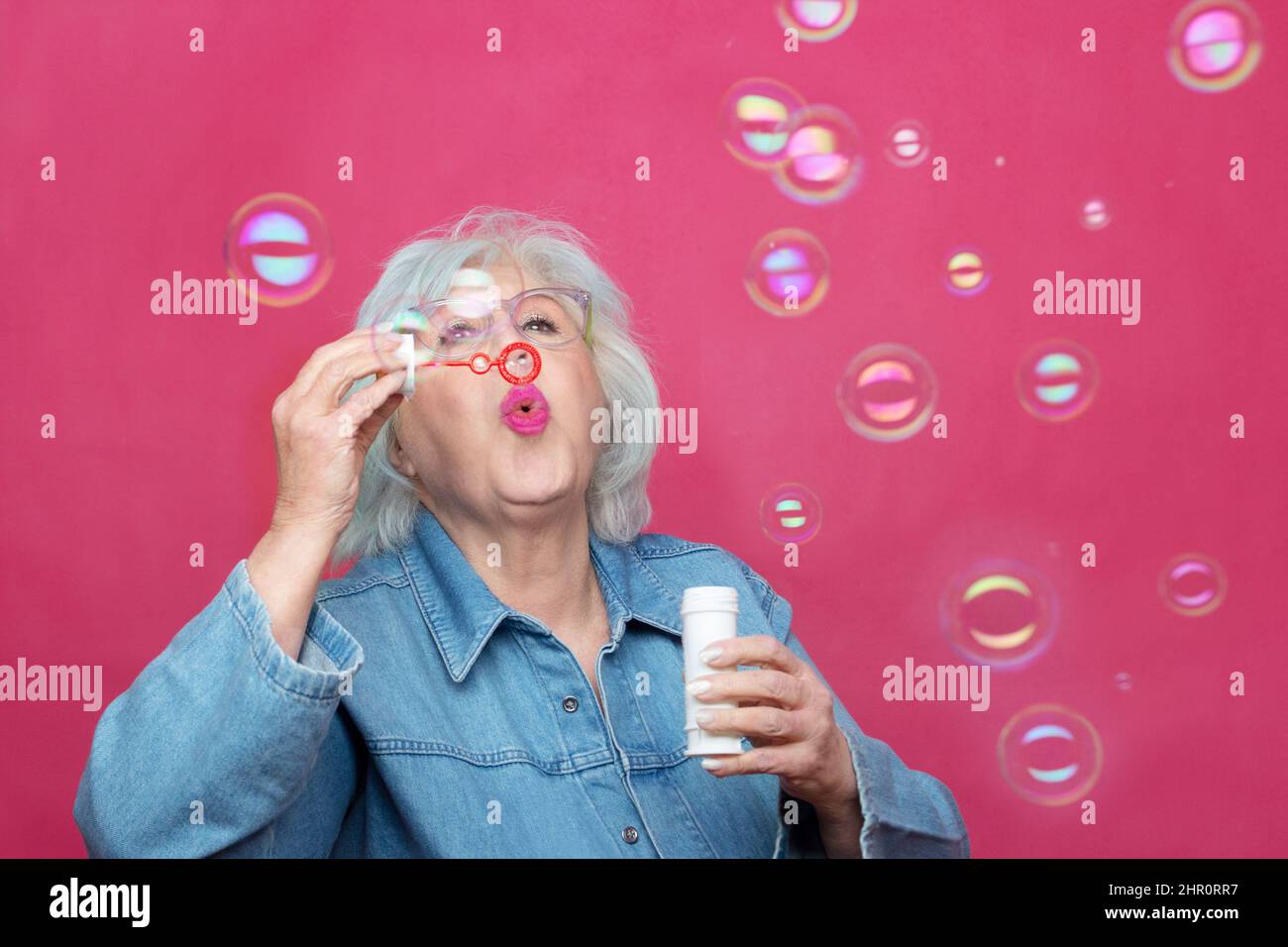 grey haired senior woman blowing soap bubbles on a plain background Stock Photo