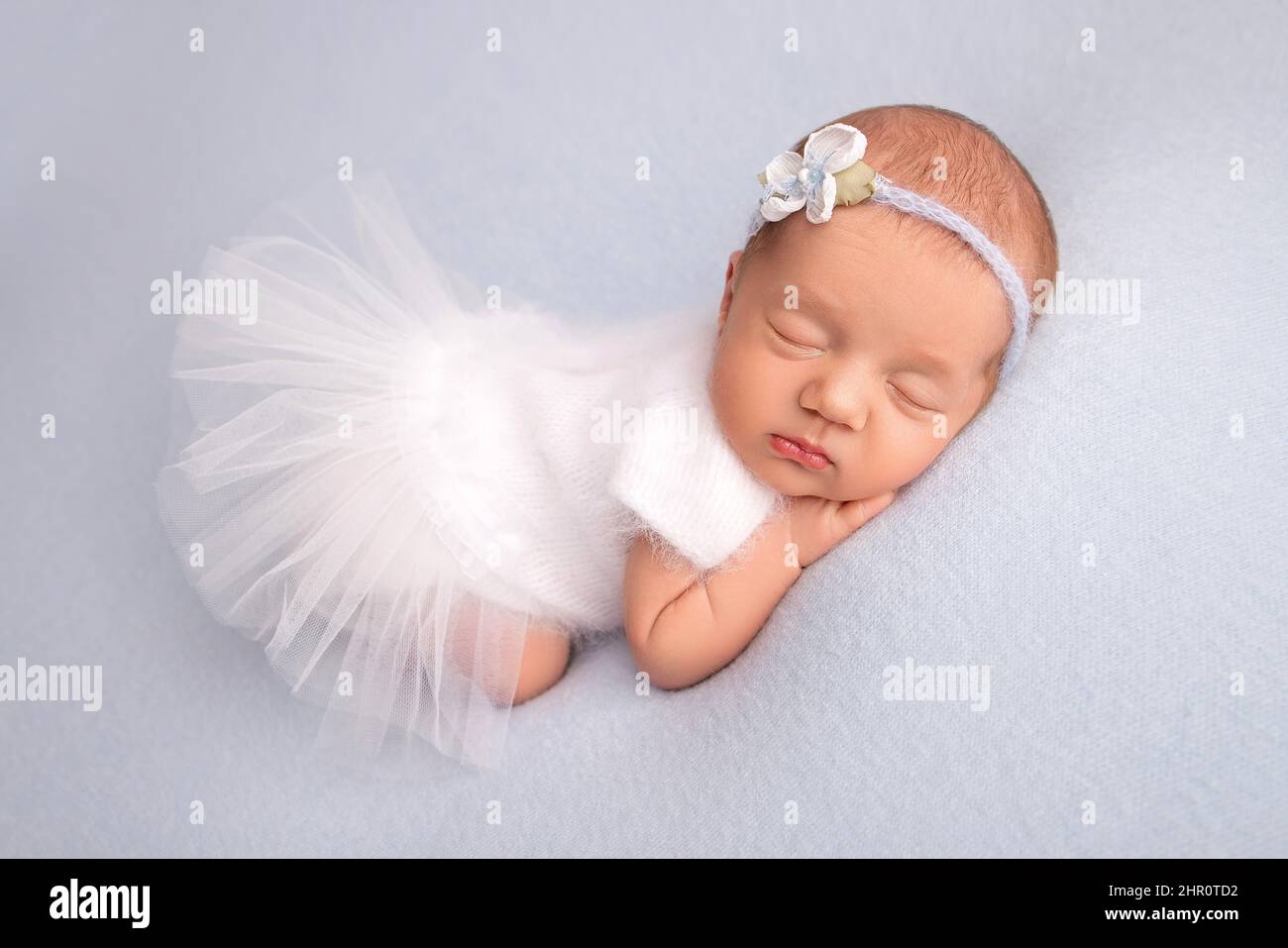 Sleeping newborn girl in a white ballet dress with a white bandage and a blue flower.Portrait of a newborn ballerina. Stock Photo