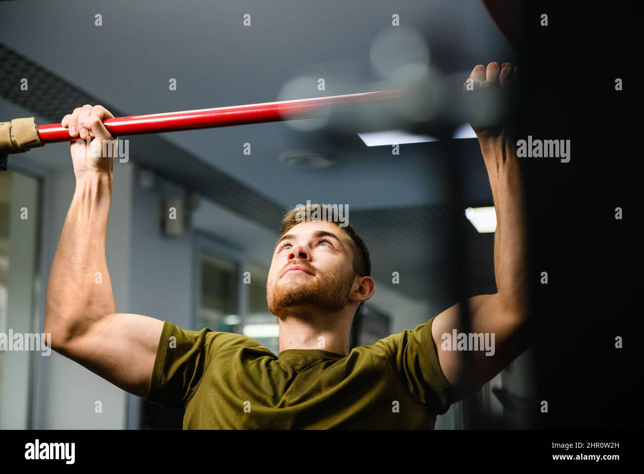 Young man making hands exercises of chin pull up at gym interior, fit