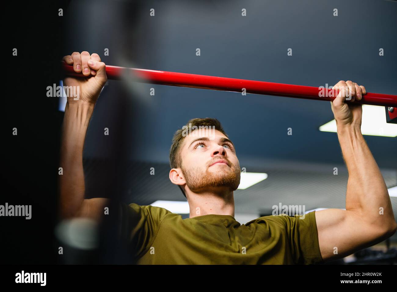 Young man making hands exercises of chin pull up at gym interior, fit strong male during workout indoors Stock Photo