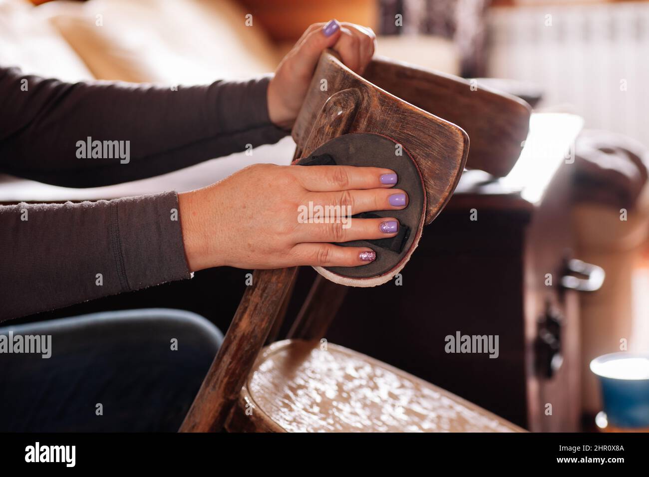 Closeup of lady removing old layer of paint and sanding surface of stool with sandpaper in home workshop. Sustainable practices. Reuse of old things Stock Photo