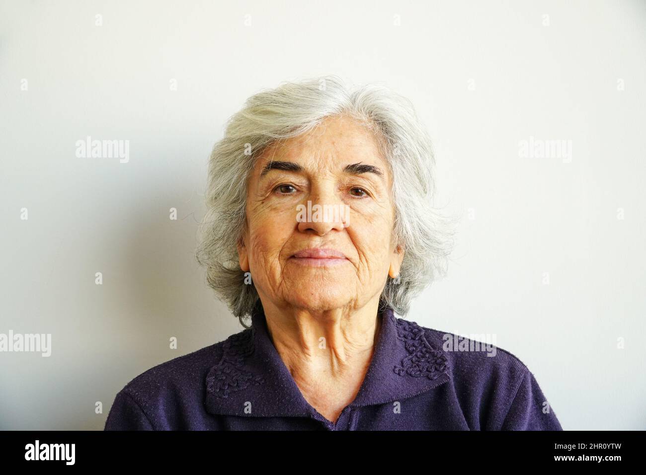 Portrait of old smiling woman in seventies. Old woman with green eyes looking at camera. Elderly person smiling peaceful. Senior woman portrait. Stock Photo