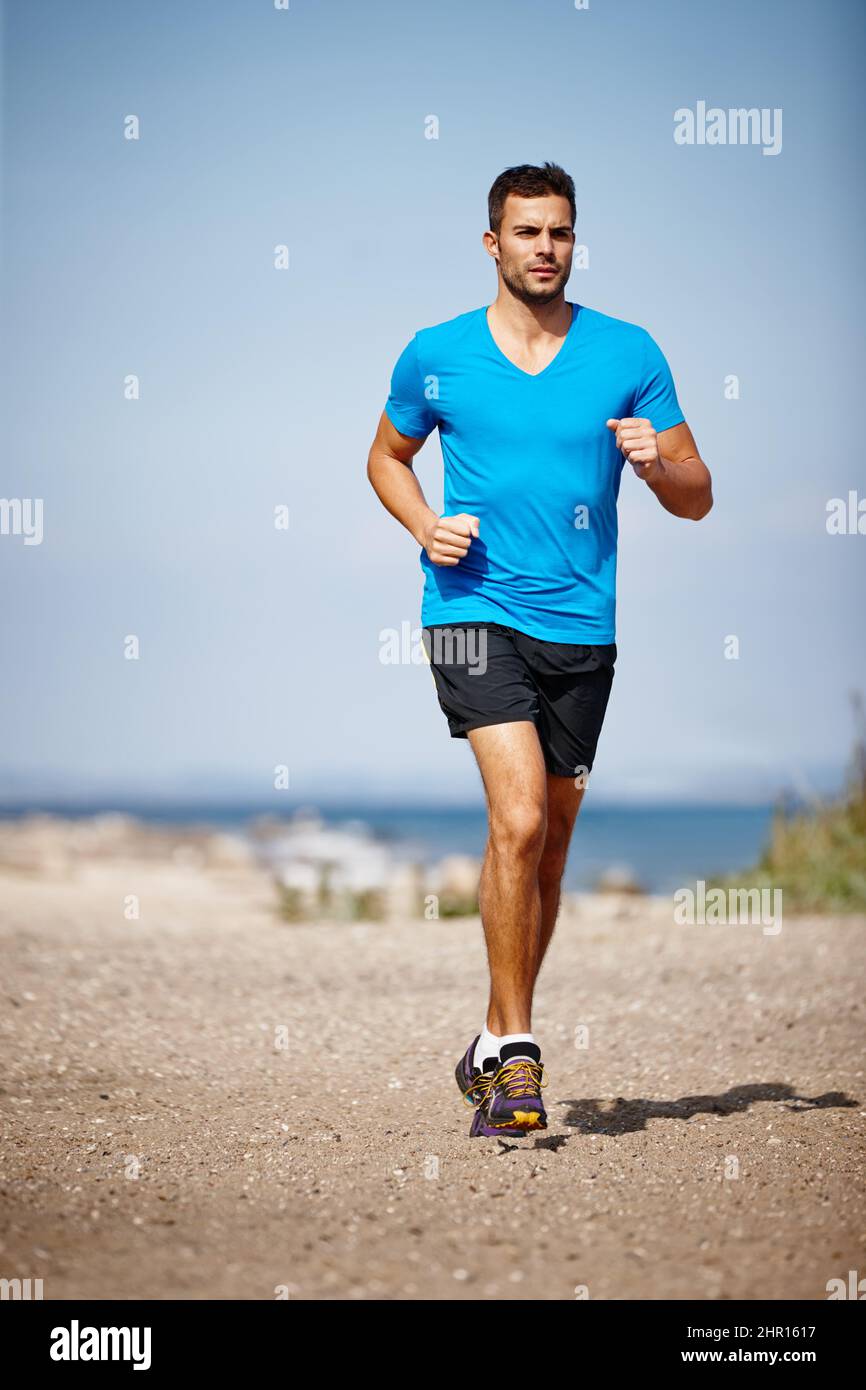 Running keeps me fit. Shot of a handsome young man running on the beach. Stock Photo