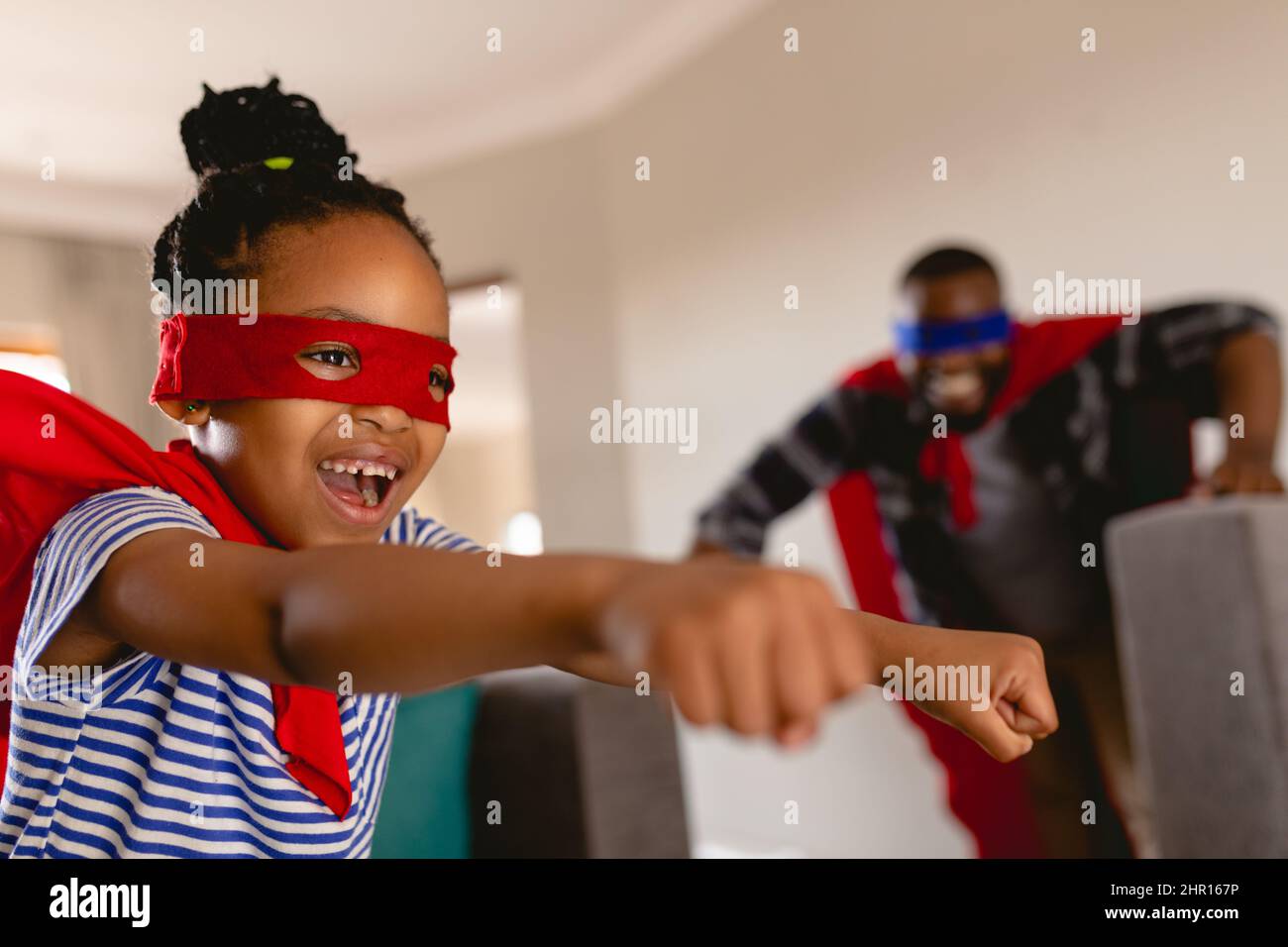 Happy african american girl wearing superhero costume flying in front of father playing at home Stock Photo