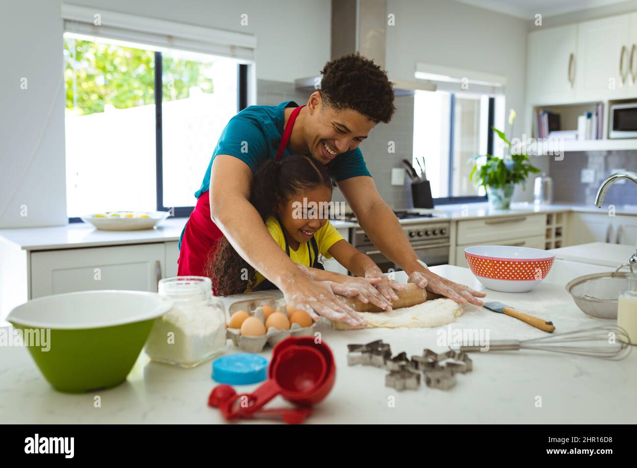 Happy biracial man assisting daughter in rolling dough on counter in kitchen Stock Photo