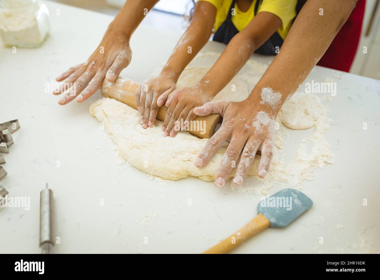 Midsection of biracial father and daughter flattening dough with rolling pin on kitchen counter Stock Photo