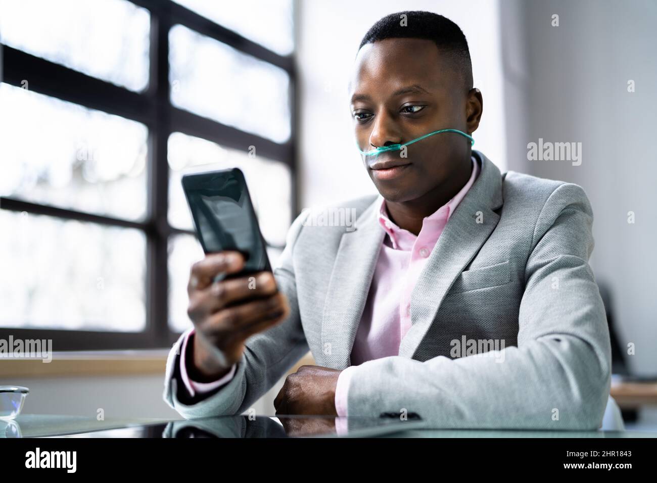 African Man Using Phone With Nasal Oxygen Cannula. Medical Condition Stock Photo
