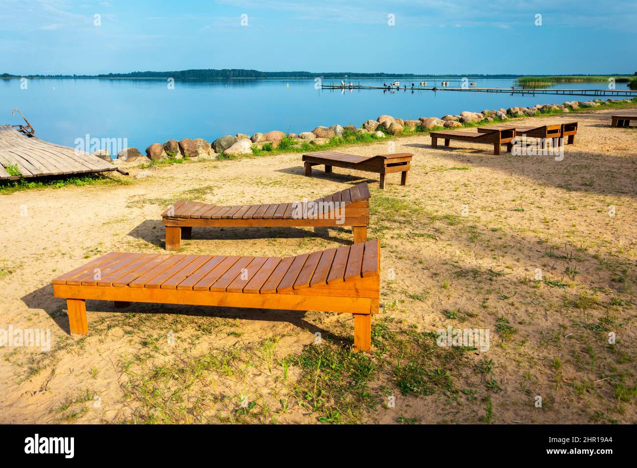 A row of wooden sun beds on the beach. Sunlight, water and sand. Wooden
