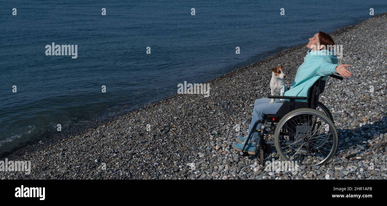 Happy woman in a wheelchair on the seashore raised her hands and imagines that she is flying.  Stock Photo