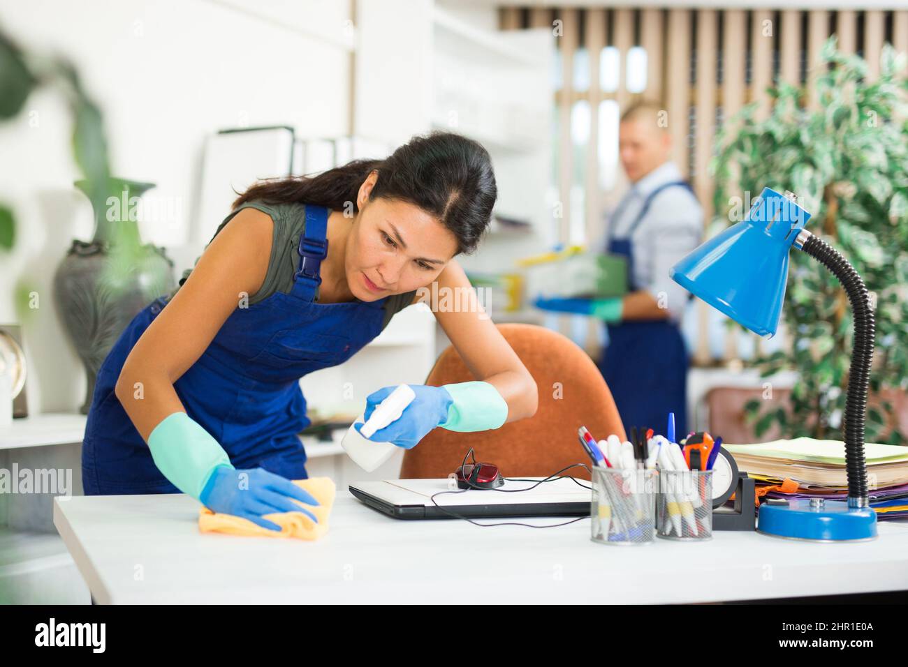 Female janitor dusting furniture in office with cleaning equipments