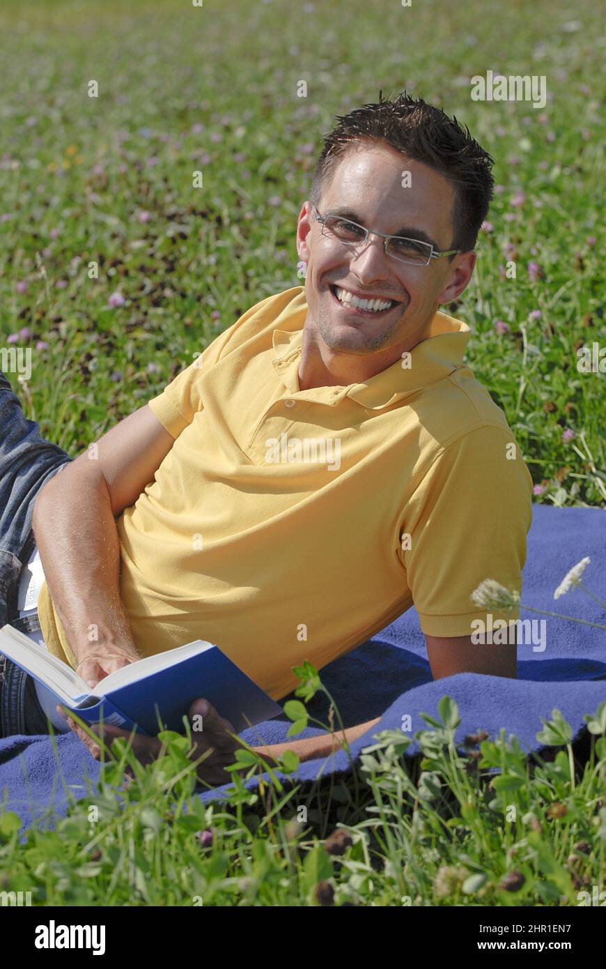 happy man lying in a meadow with a book , Germany Stock Photo