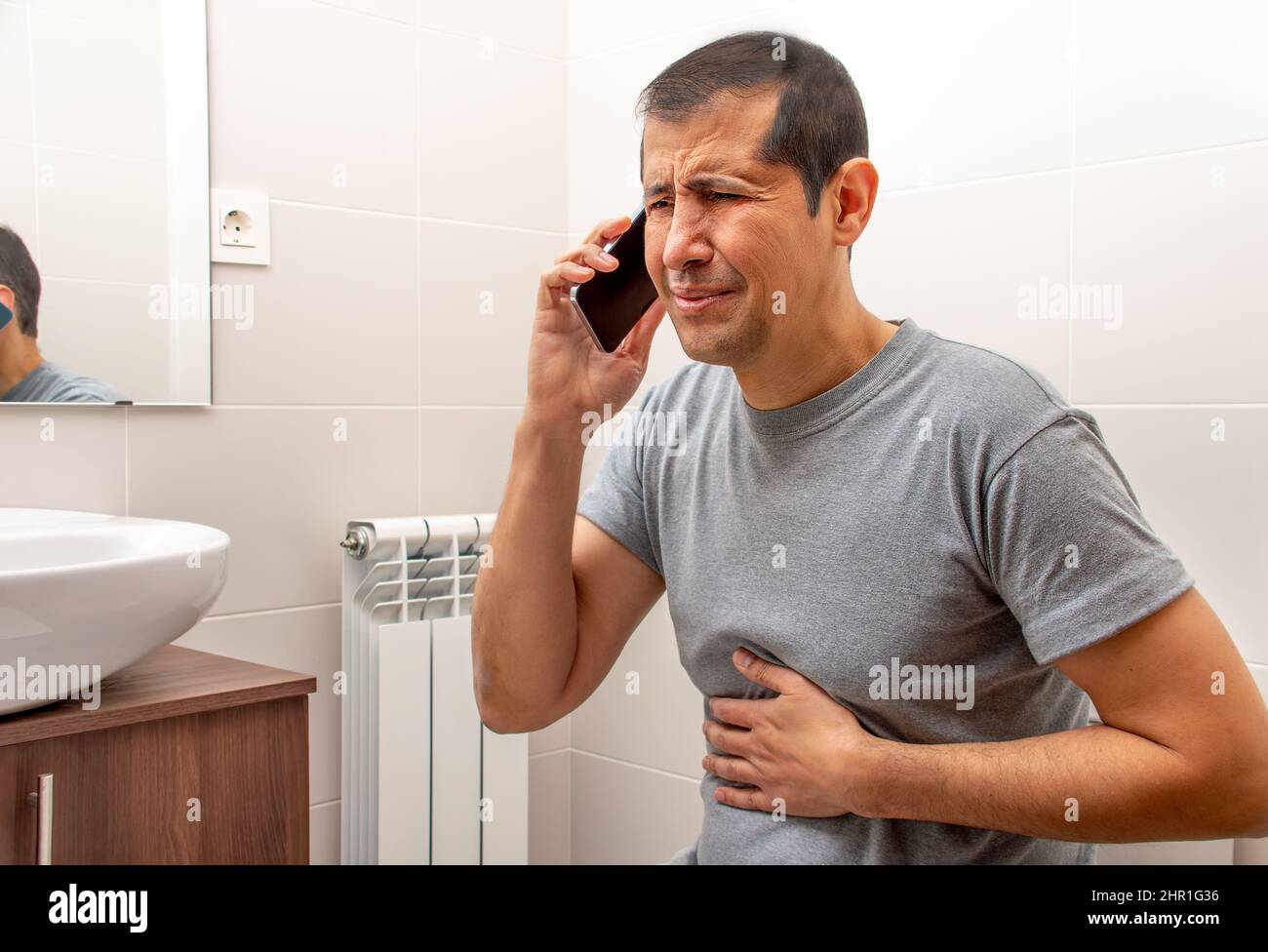 Cropped shot of an man sitting on the toilet in a bathroom suffering from stomach cramps and calling medical assistance on phone Stock Photo