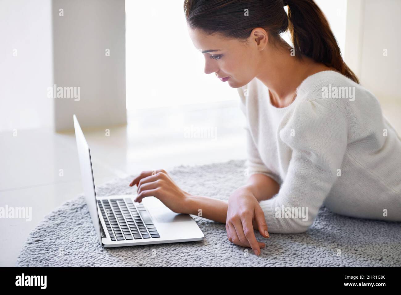 My morning dose of social networking. A beautiful young woman lying on her floor at home and using a laptop. Stock Photo