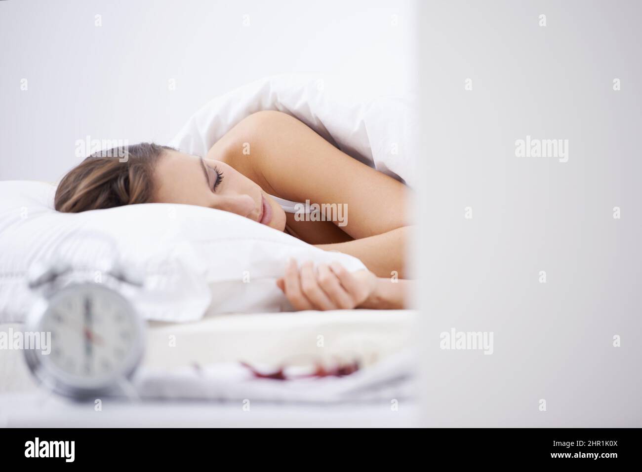 Getting her 8 hours. A woman sleeping in her bed with an alarm clock in the foreground. Stock Photo