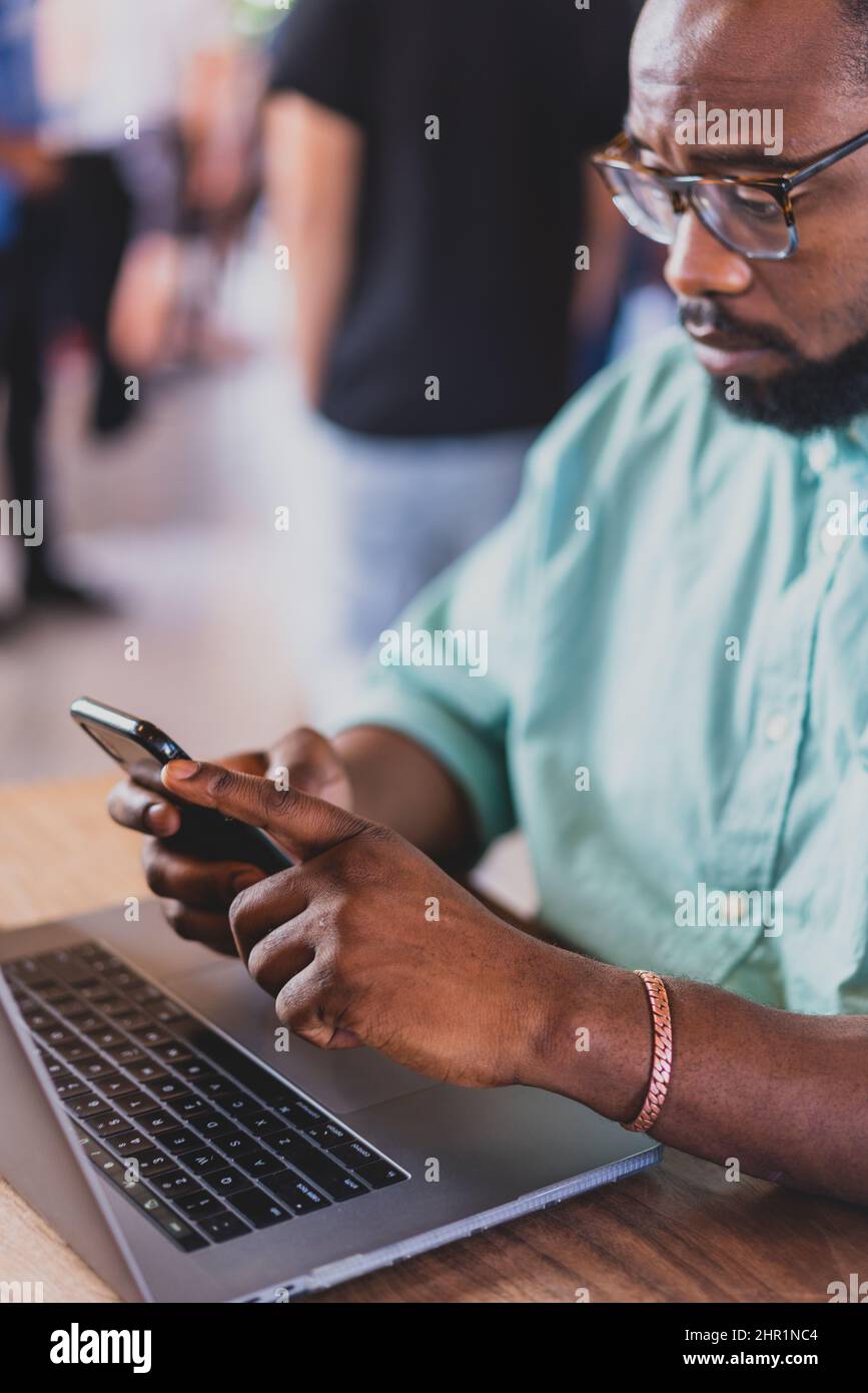 closeup of black man looking at cell phone with laptop Stock Photo