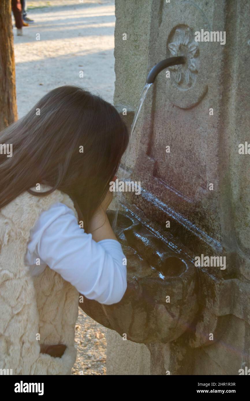 Kids drinking fresh water on outside fountain after playing outside. Public spaces water streams, catching water by hand to drink. Stock Photo