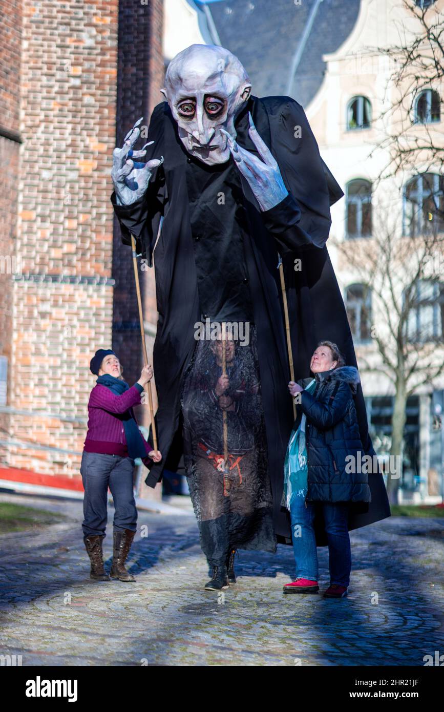 Wismar, Germany. 23rd Feb, 2022. Members of the Kulturmühle Wismar association are out and about in the old town with the four-meter-high 'Nosferatu' figure. For the summer, a street theater spectacle centered around the eerie Count Nosferatu is being staged in Wismar at original locations of the horror classic in the old town. To mark the 100th anniversary of Friedrich Wilhelm Murnau's silent film of the same name, the association is planning to stage silent film scenes with six large puppets in front of historical backdrops. Credit: Jens Büttner/dpa-Zentralbild/dpa/Alamy Live News Stock Photo