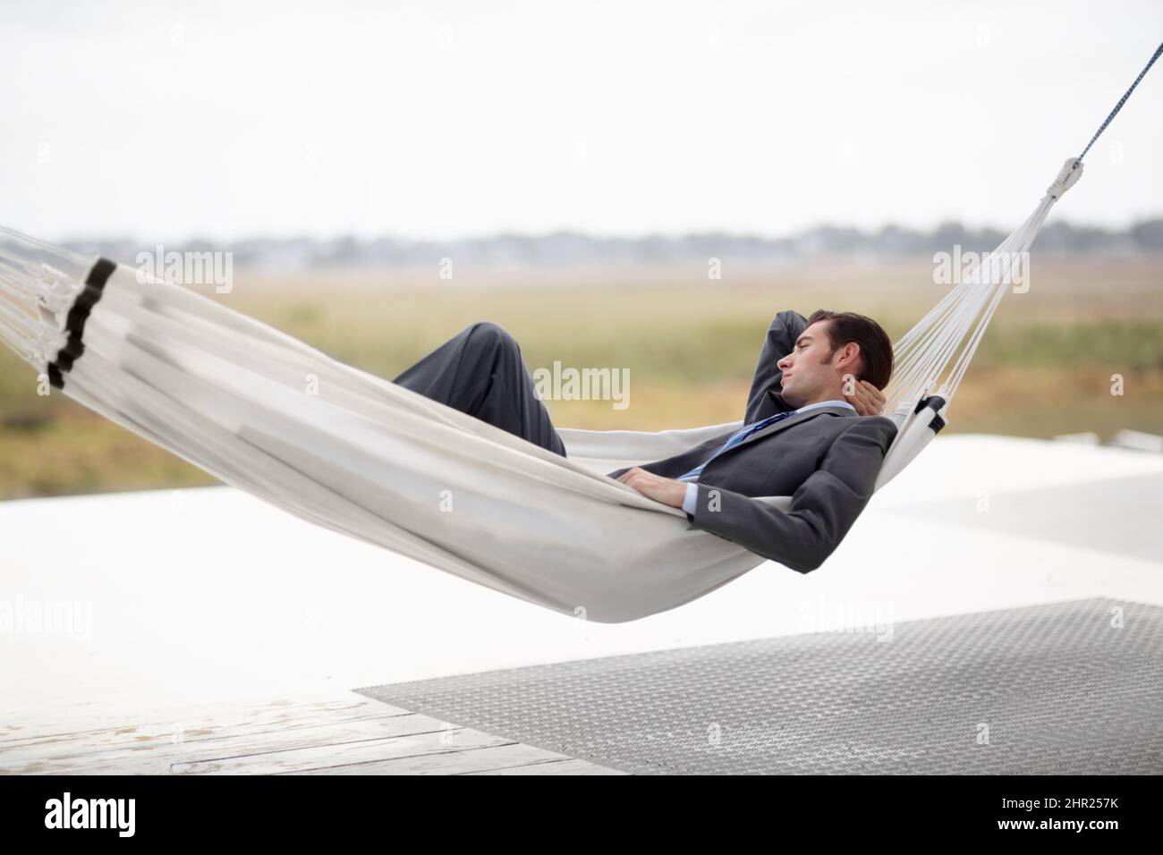 Taking in the landscape. A young executive in a suit taking in the landscape from a hammock. Stock Photo