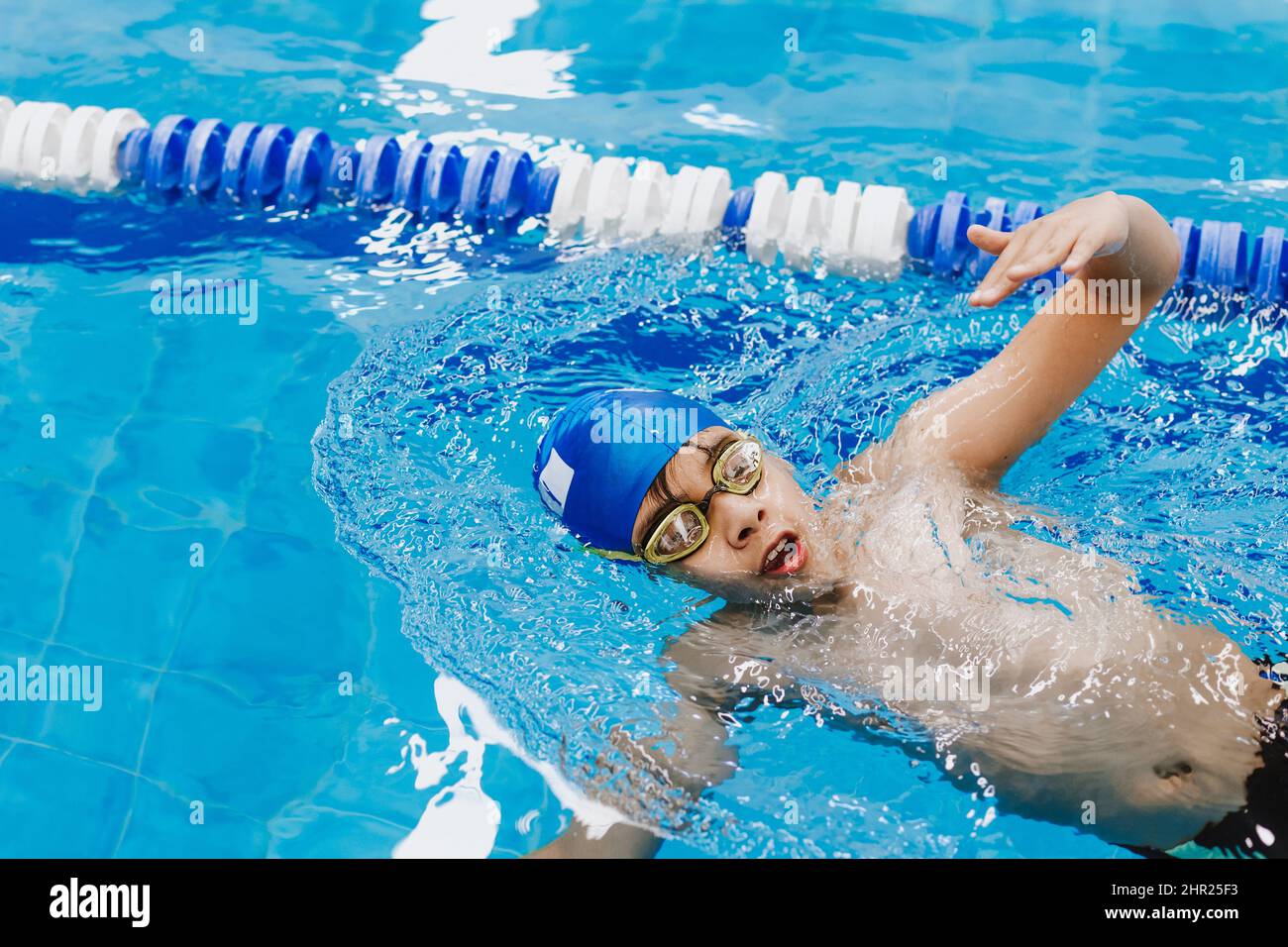 latin child boy swimmer wearing cap and goggles in a swimming training holding On Starting Block In the Pool in Mexico Latin America Stock Photo