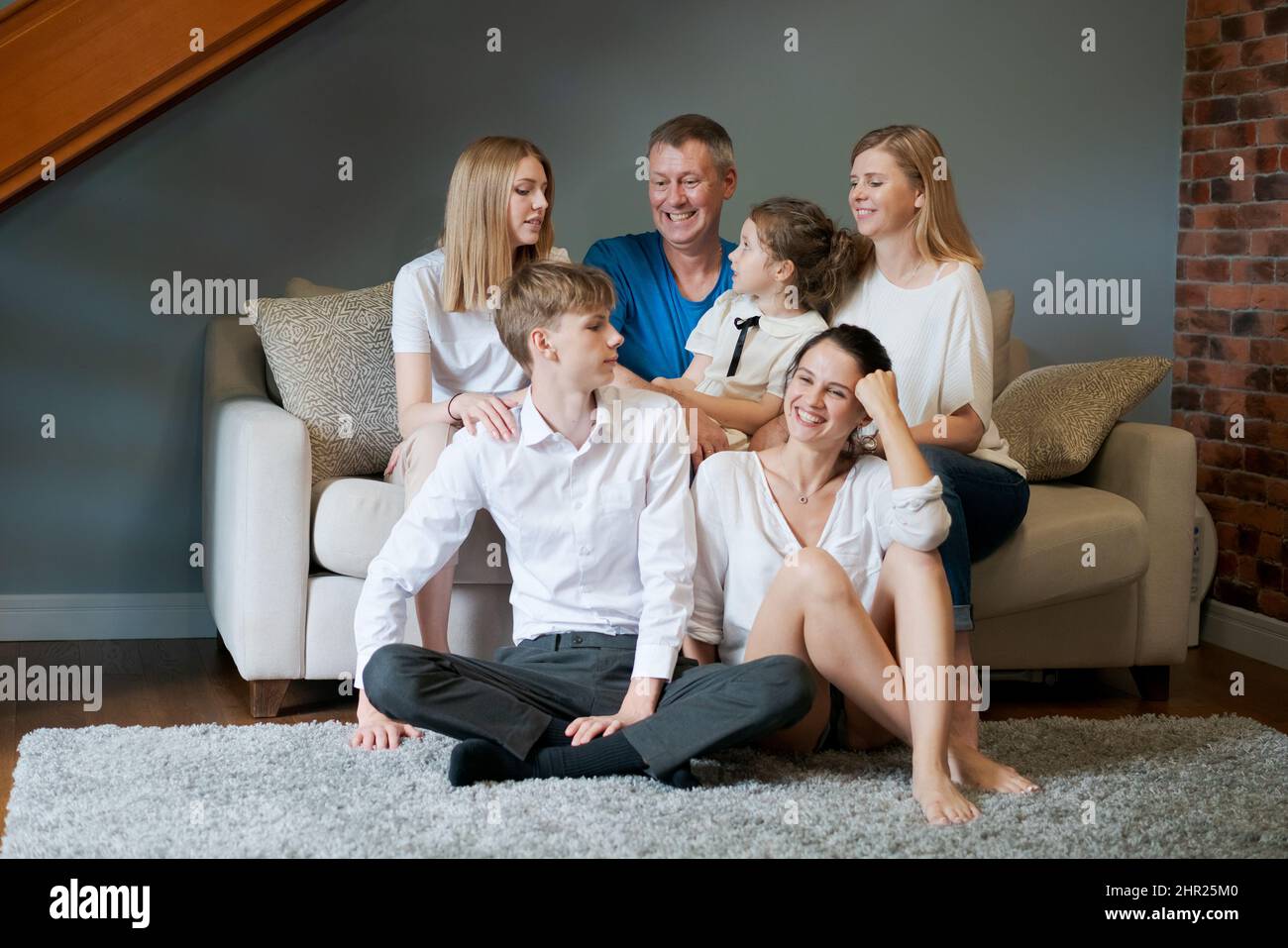 Large family several generations with children relaxing on couch in living room, smiling and chatting, spending time together at home. Happy time with a friendly family Stock Photo