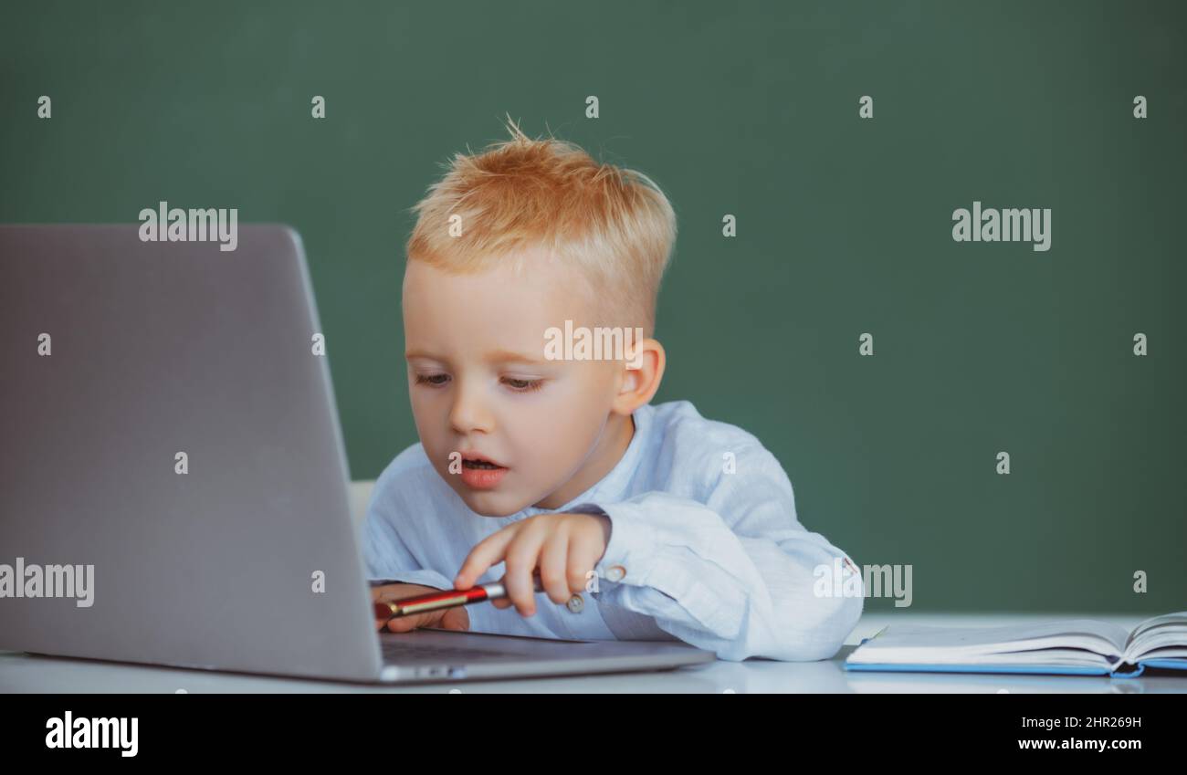 School child using digital pc laptop in class. Portrait of funny pupil of primary school study programming. Funny blonde pupil on blackboard. Stock Photo