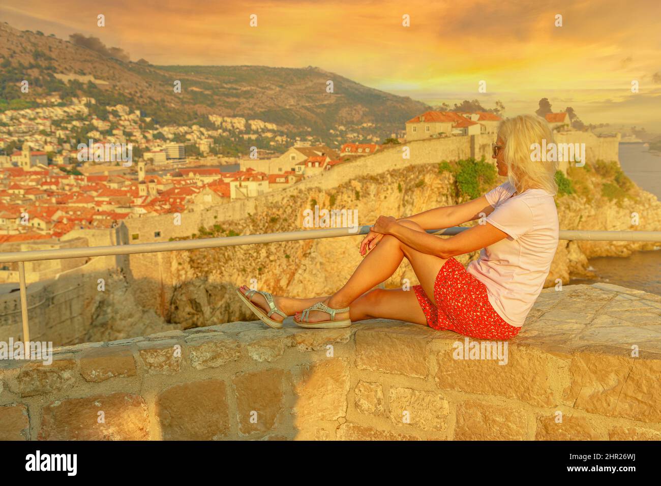 Woman resting at sunset on Lovrijenac fortress top walls, over the West Harbour. Dubrovnik cityscape with Fort Bokar in Croatia. historic city in Stock Photo