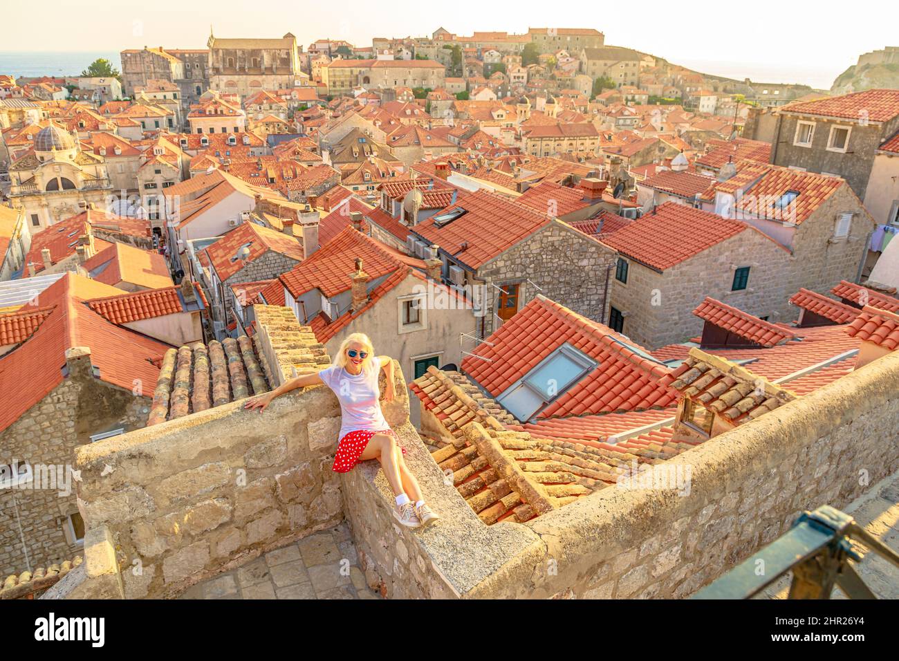 Aerial view of a woman on Dubrovnik walls at sunset in Croatia. View of Fort Lovrijenac fortress and church Crkva sv. Vlaho Saint Biagio of Dubrovnik Stock Photo