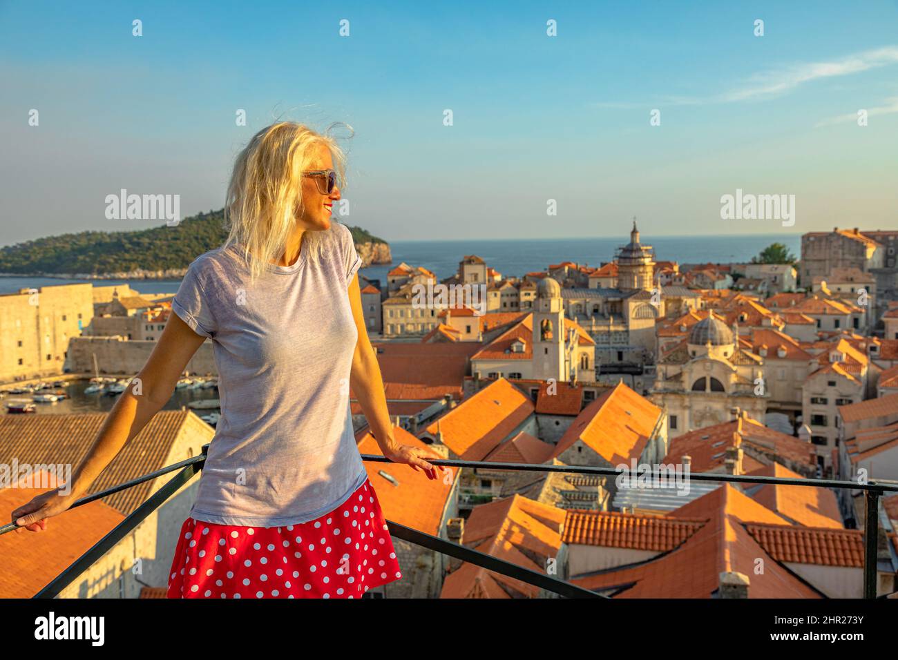 Woman at sunset on Dubrovnik walls of Croatia. View of Crkva sv. Vlaho church and Dubrovnik Cathedral of the Assumption of the Virgin Mary. in Stock Photo