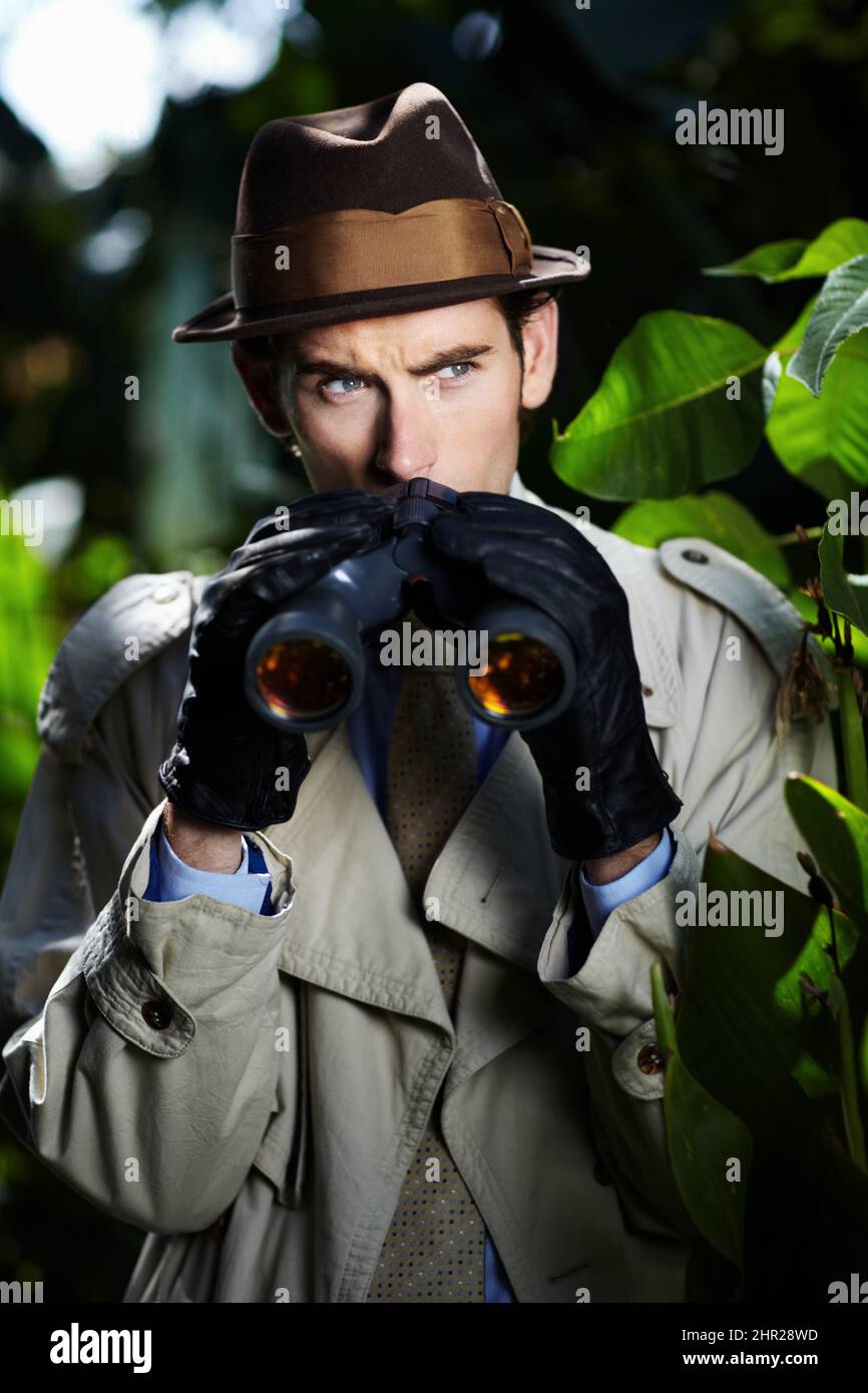 Checking up on you.... Private investigator using binoculars to spy on someone from the bushes. Stock Photo