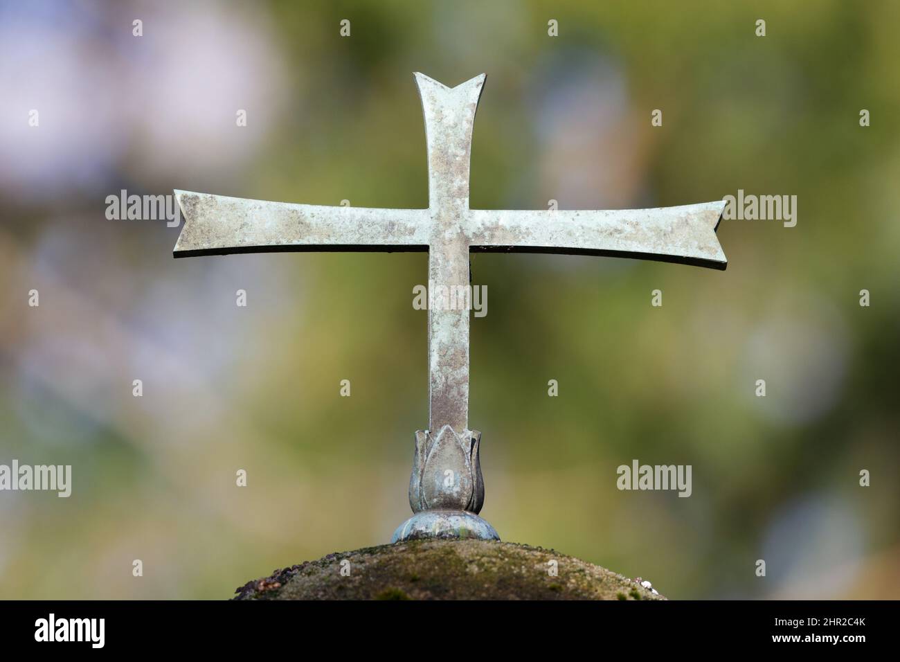 metal cross on a gravestone of a cemetery in front of blurred green background Stock Photo