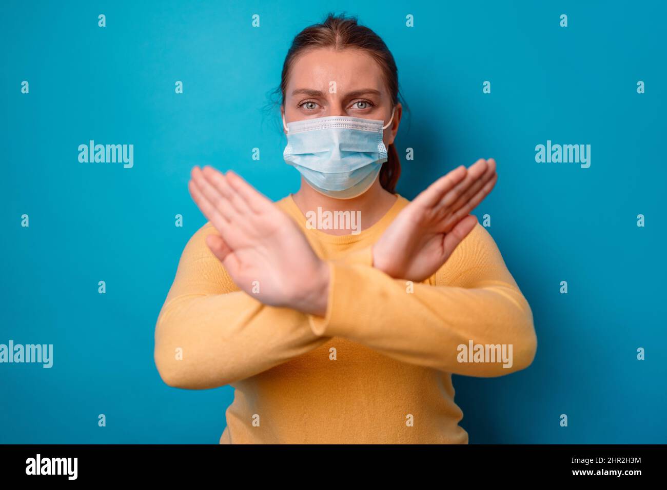 Portrait of caucasian woman in yellow sweater crossing hands makes stop gesture, demonstrates rejection isolated over blue background with copy space Stock Photo