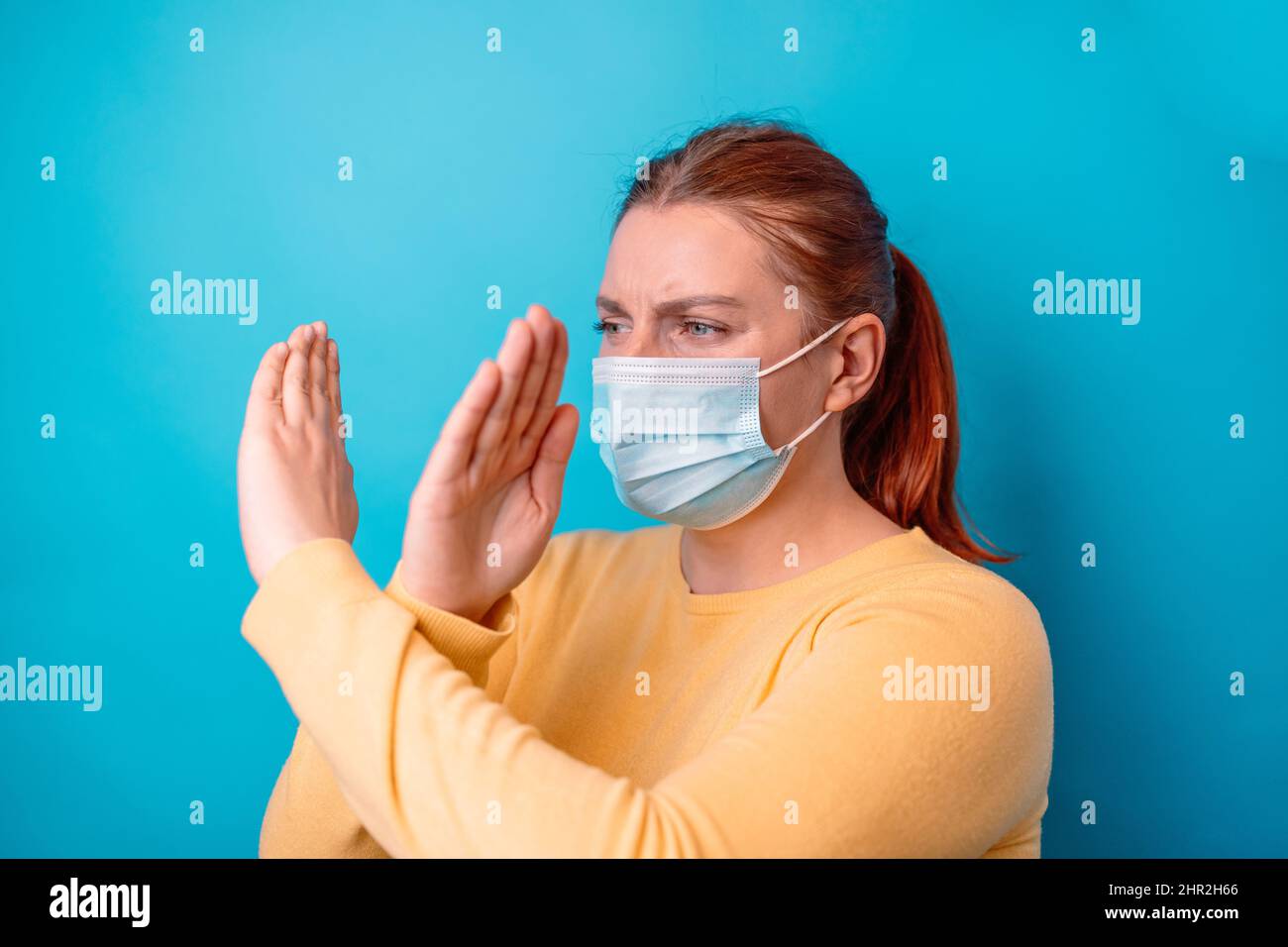Angry caucasian 20s woman in yellow sweater crossing hands makes stop gesture, demonstrates rejection isolated over blue background. Stock Photo