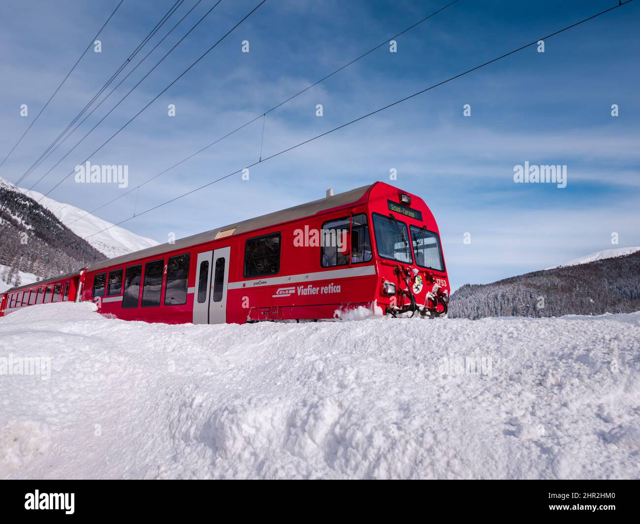 Cinuos-Chel, Switzerland - February 3, 2022: Red train of Viafier retica riding between Chur and Tirano in Italy and crossing snow covered landscape a Stock Photo