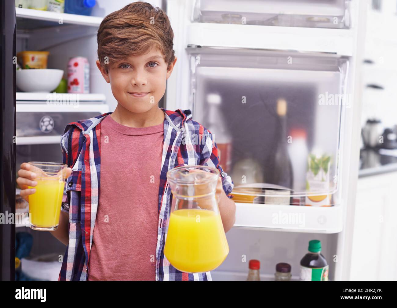 Some goodness to quench the thirst. Shot of a young boy standing in front of the fridge with some orange juice. Stock Photo