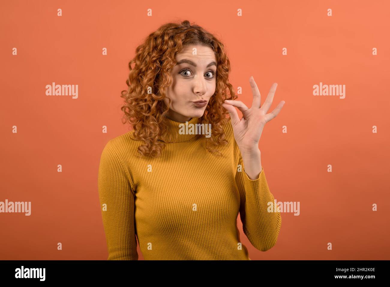Young and attractive Caucasian redhead girl smoking a cigarette isolated on orange studio background. Stock Photo