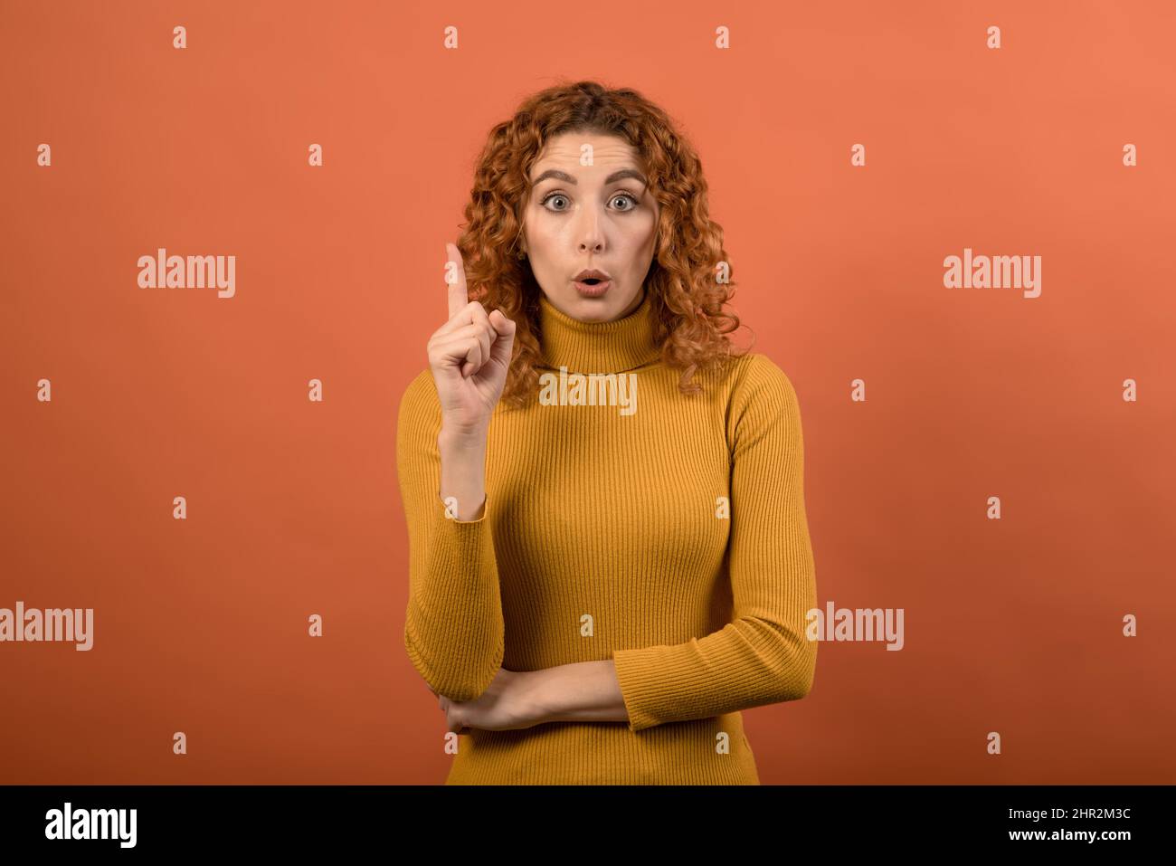 Attractive and young redhead Caucasian girl has an idea isolated on orange studio background. Stock Photo