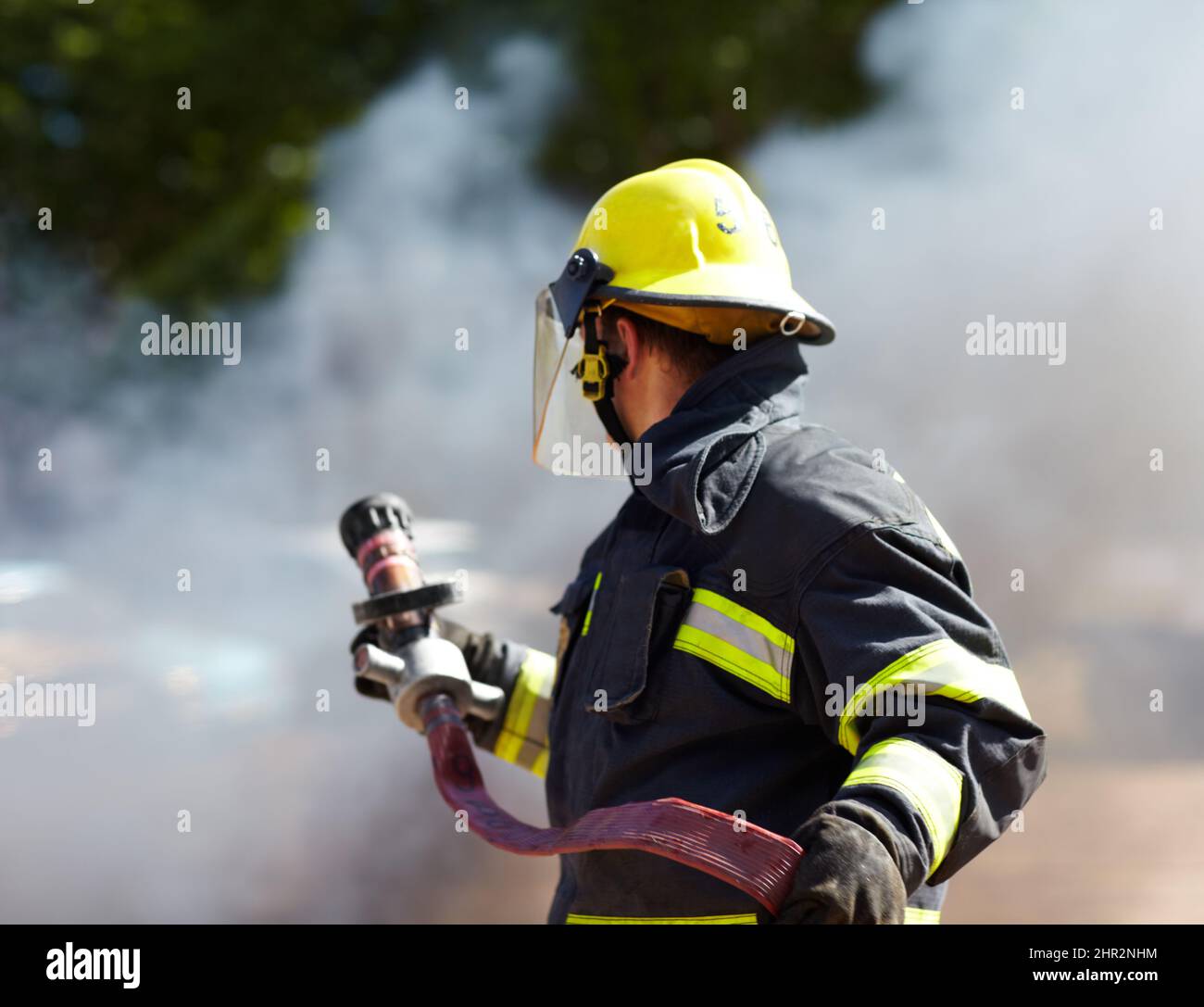 Hes got the situation under control. A caucasian fireman holding a hose and surrounded by the smoke from the fire hes just extinguished. Stock Photo