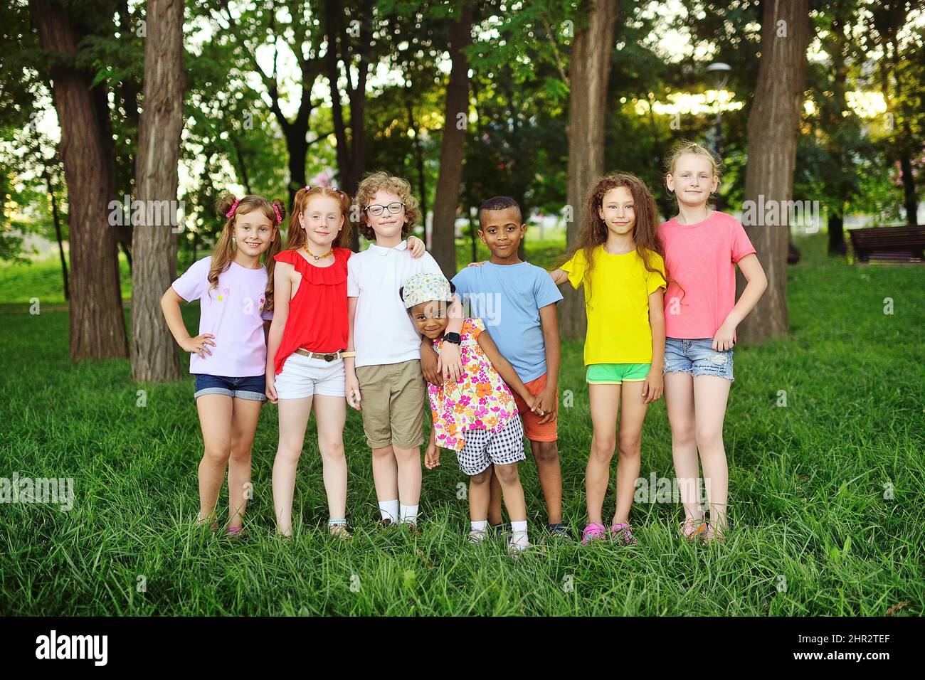 group of preschoolers of different races hug and smile against the background of greenery and a park. Children Protection Day. Stock Photo