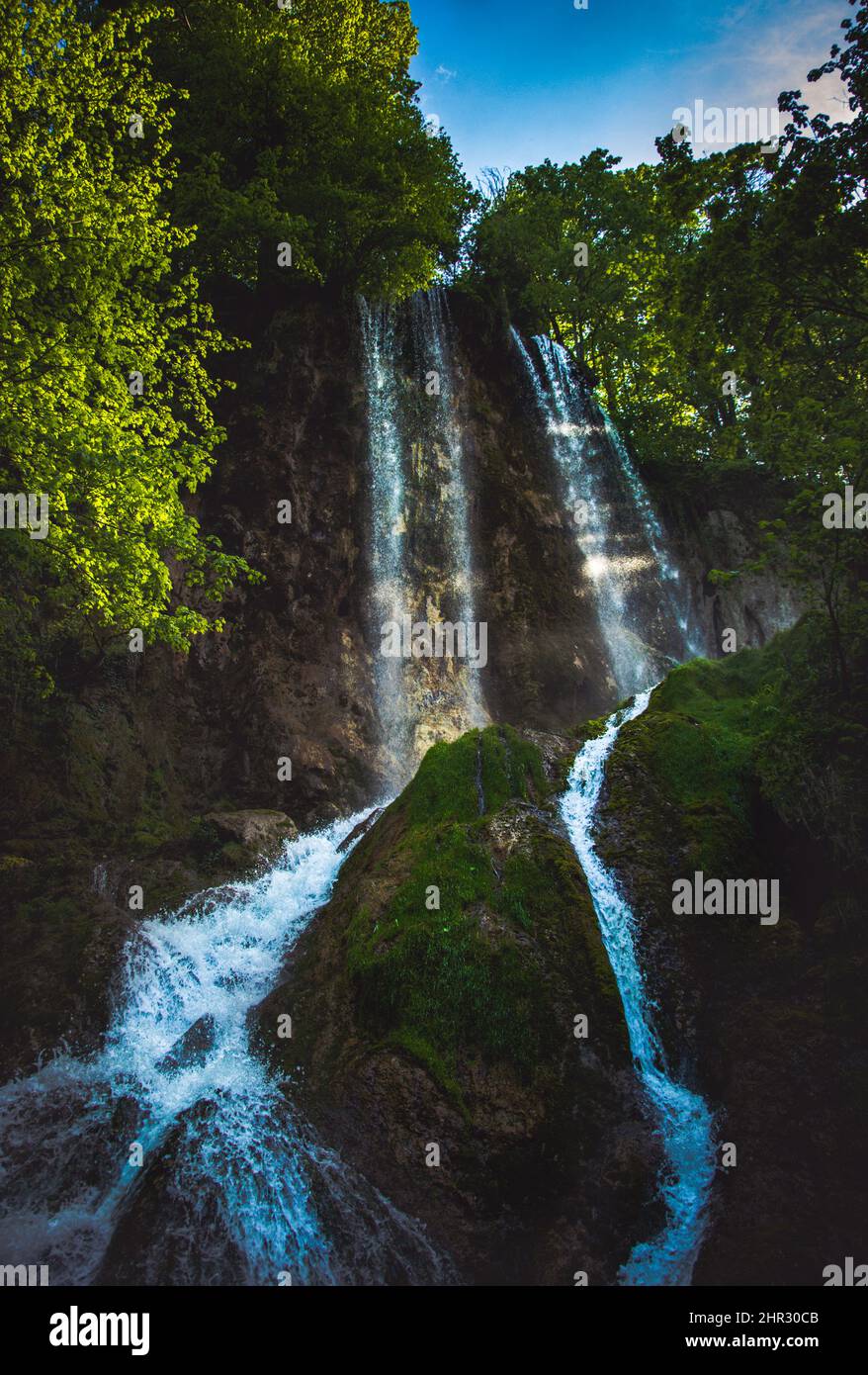 Vertical of a waterfall flowing down the rocks covered with moss among ...