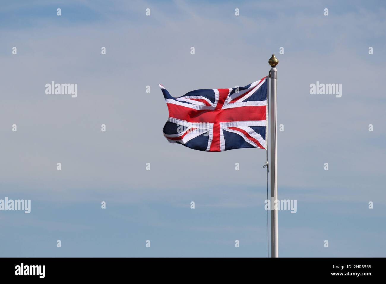 Union Jack Flag on a pole flying against sky background Stock Photo