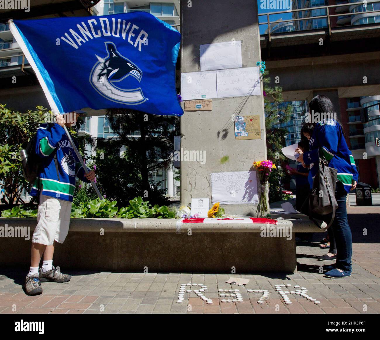 Calvin Ng, left, holds a Vancouver Canucks flag as Heidi Mak, right, pauses at a makeshift memorial for former Canucks hockey player Rick Rypien outside Rogers Arena in Vancouver, B.C., on Tuesday August 16, 2011. Rypien, who signed a one-year deal with the Winnipeg Jets in July, was found dead at his Alberta home on Monday. THE CANADIAN PRESS/Darryl Dyck Stock Photo