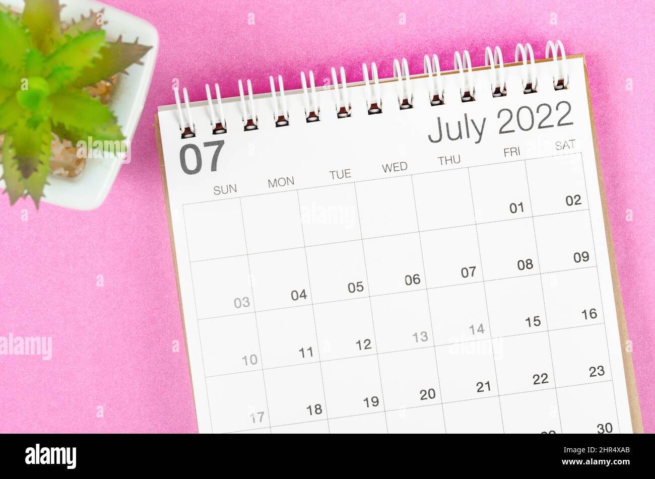 The July 2022 desk calendar with plant pot on pink background. Stock Photo