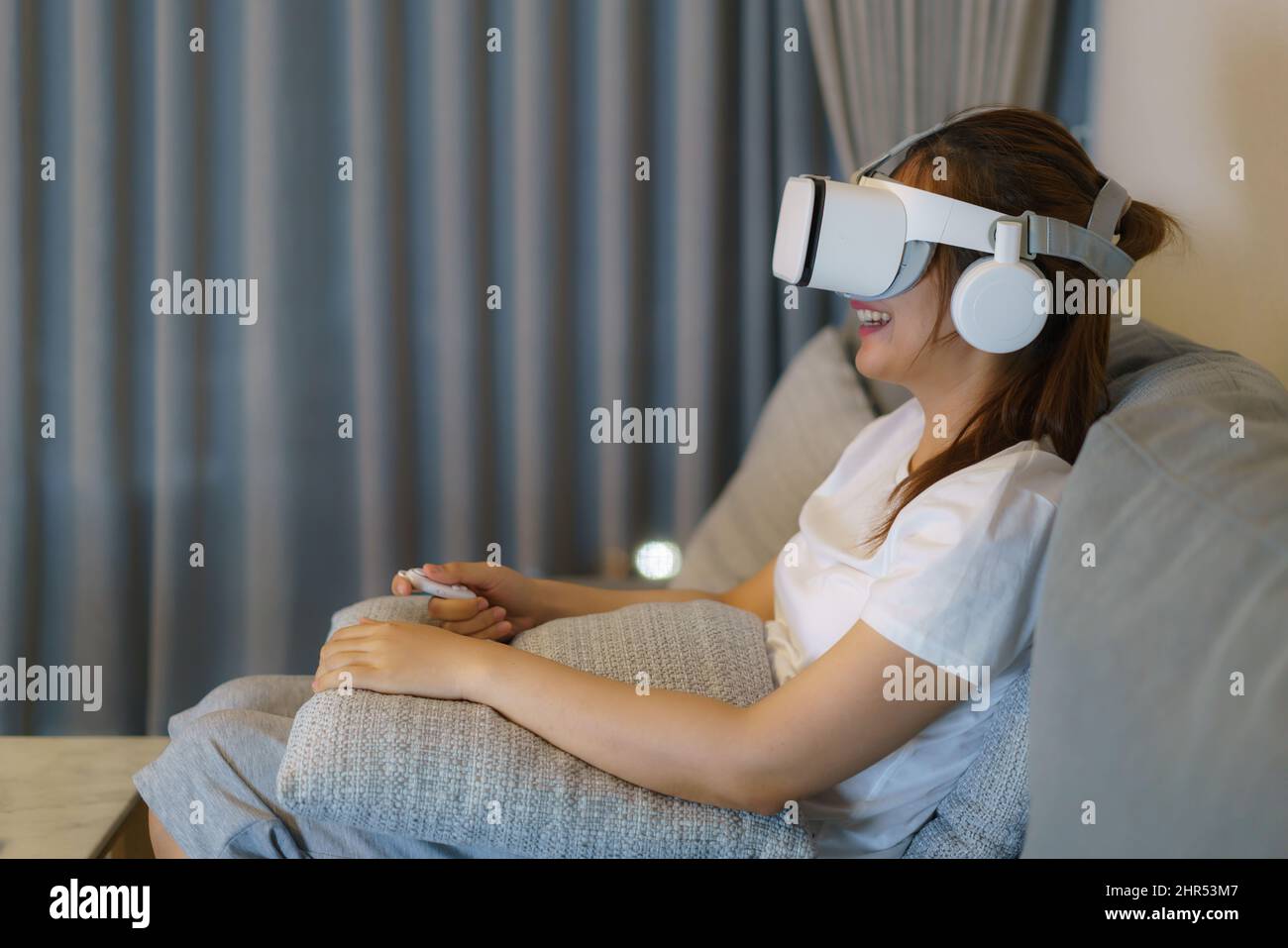Asian woman enjoy watch 3d video and wear virtual reality headset in living room in home at night. Stock Photo