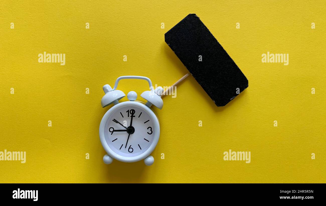 Alarm clock on yellow background with small black signage. Copy space