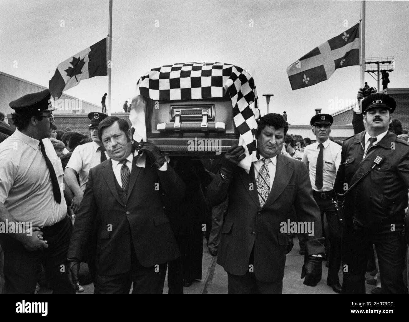 Canada and Quebec flags fly at half-mast as a casket draped in a checkered flag containing the body of Canadian racing driver Gilles Villeneuve leaves the Cultural Centre, Berthierville, Que., May 12, 1982, for funeral series at his hometown church. Villeneuve, 32, was killed May 8, 1982. THE CANADIAN PRESS/UPC/Bernard Brault Stock Photo