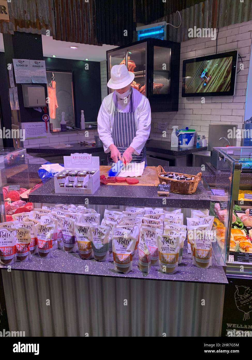 Farndon Fields farm shop Market Harborough Leicestershire England butcher mask apron cutting working white hat covered up tv cabinet basket Stock Photo