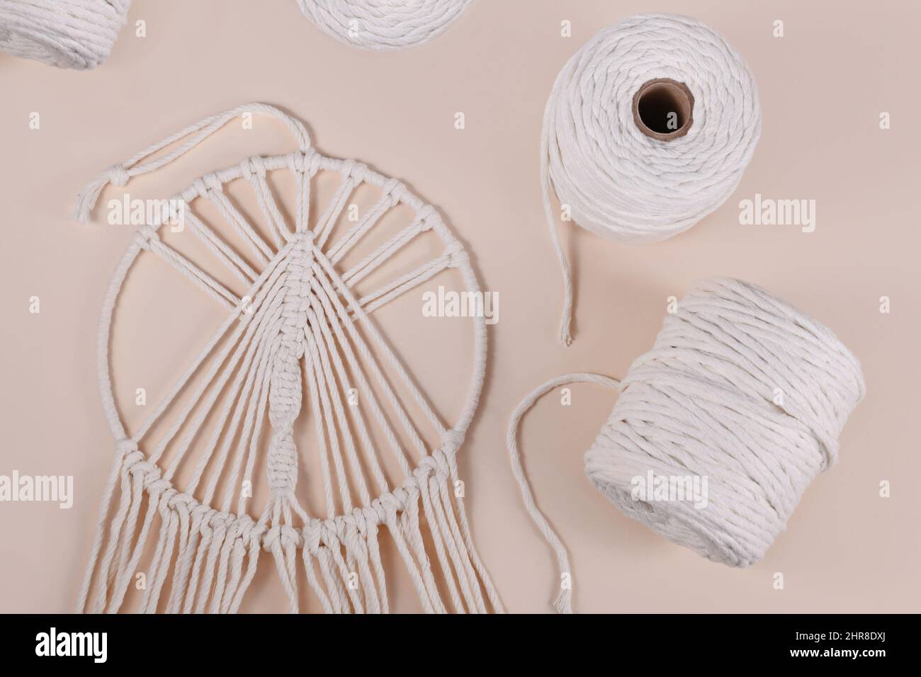 Cotton macrame cord and finished wall hanging object on beige background Stock Photo